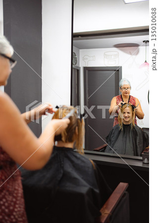 Hairdresser cutting client's hair reflecting in mirror Hairdresser cutting client's hair reflecting in mirror 135010088