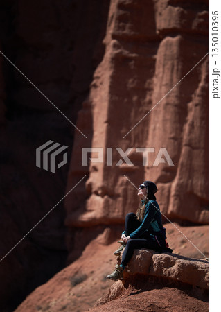 Woman traveler sits on red rock, enjoying vast landscape. Adventure travel 135010396