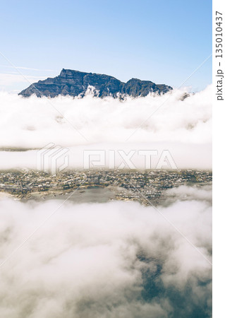 Mountains peeking through thick layer clouds with city partially visible below Mountains peeking through thick layer clouds with city partially visible below 135010437
