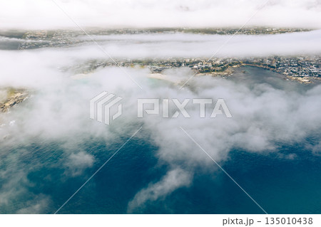 Aerial view of coastal city partially covered by low-lying clouds over the ocean Aerial view of coastal city partially covered by low-lying clouds over the ocean 135010438