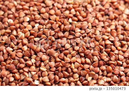Brown grains of uncooked buckwheat groats close up. Healthy food ingredient Brown grains of uncooked buckwheat groats close up. Healthy food ingredient 135010473