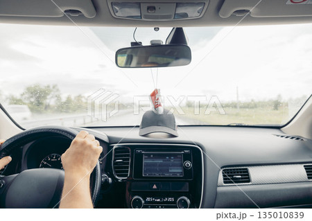 driver holds steering in car on rainy road, windshield wipers working, dashboard screen visible, front view of travel journey with mirror and hanging decoration, transport, lifestyle driver holds steering in car on rainy road, windshield wipers working, dashboard screen visible, front view of travel journey with mirror and hanging decoration, transport, lifestyle 135010839