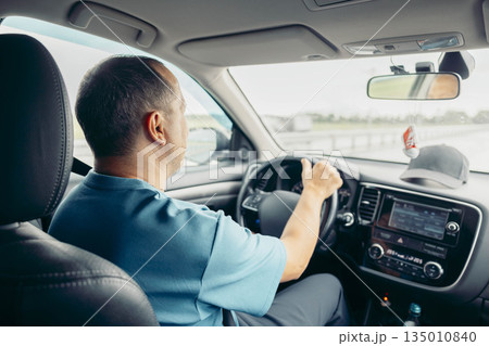 A middle-aged Caucasian man with short hair drives a car on a highway. He appears focused and relaxed, enjoying the journey. A middle-aged Caucasian man with short hair drives a car on a highway. He appears focused and relaxed, enjoying the journey. 135010840