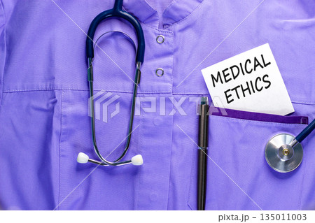 Medical ethics symbol. Concept words Medical ethics on beautiful white card. Stethoscope and pen. Beautiful medical uniform. Healthy lifestyle medical ethics concept. 135011003