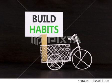 Build habits symbol. Concept word Build habits on beautiful white paper. Beautiful wooden clothespin. Miniature black bicycle. Beautiful orange background. Business build habits concept. Copy space. 135011006
