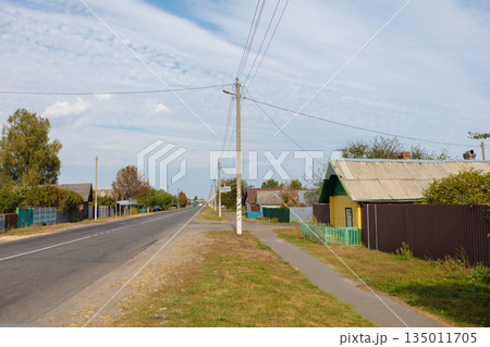 A street with a house on the right. The house is yellow. There are trees on the left side of the street A street with a house on the right. The house is yellow. There are trees on the left side of the street 135011705