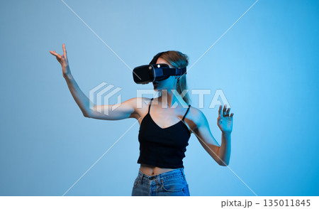 Side view of young woman using VR headset and controlling virtual interface with hand gestures, immersive technology and future digital concept 135011845