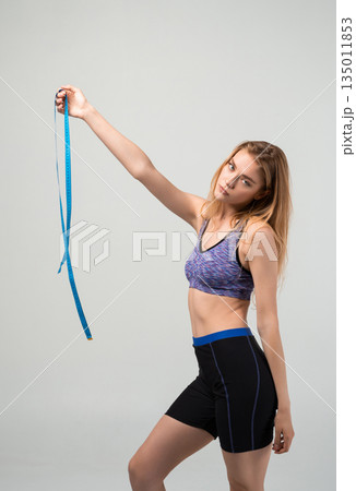 Fit young woman holding measuring tape, fitness progress, body measurement and healthy active lifestyle concept 135011853