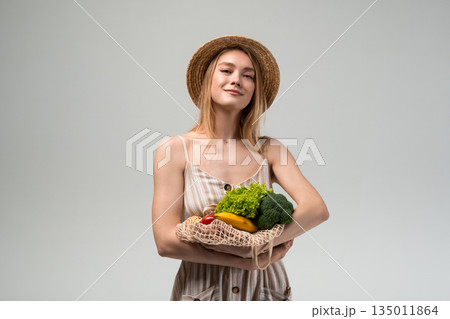 Young woman carrying reusable mesh shopping bag with groceries over shoulder, eco friendly food shopping, sustainable lifestyle, healthy nutrition and conscious consumer behavior Young woman carrying reusable mesh shopping bag with groceries over shoulder, eco friendly food shopping, sustainable lifestyle, healthy nutrition and conscious consumer behavior 135011864