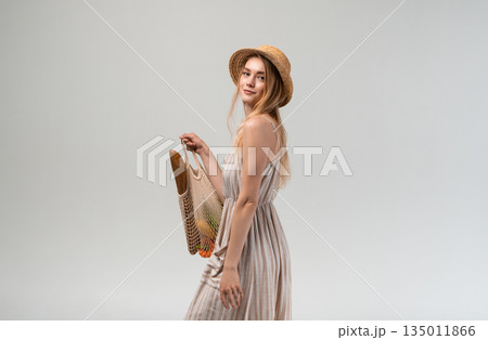 Attractive young woman carrying reusable mesh bag with groceries over shoulder, healthy food shopping concept, eco friendly lifestyle, conscious consumer behavior 135011866