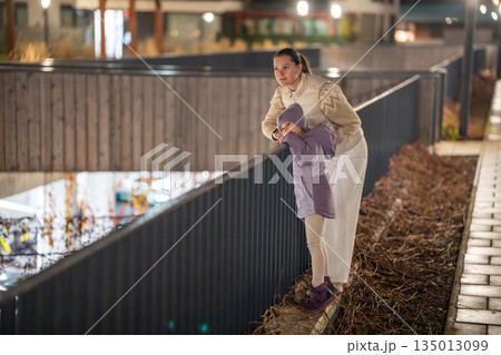 Mother lifting child to play on railing in quiet neighborhood. Fun parenting moment. 135013099