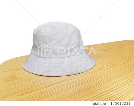 A white bucket hat on a wooden table, against a white background. A white bucket hat on a wooden table, against a white background. 135013231