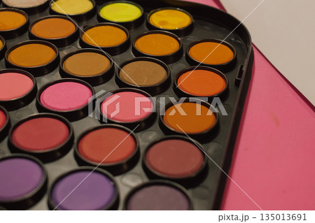 Artist's palette close-up: Bright watercolor or tempera paint cakes (pink, orange, purple) arranged on a vibrant pink background with a white sheet. Art supplies and creative background 135013691