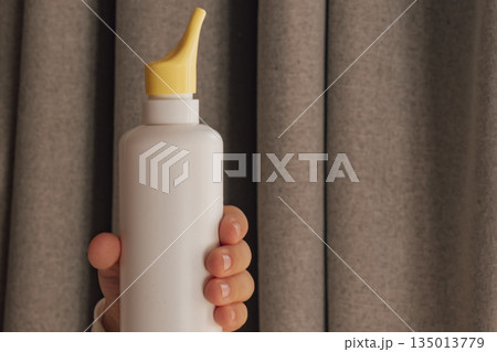 Child's hand holding a nasal spray bottle with saline solution against a soft background 135013779