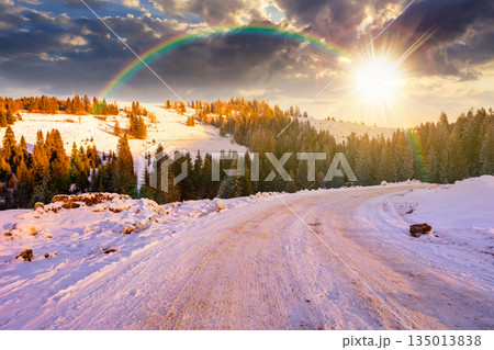 winter landscape with snow covered country road winding through fir forest in mountains at sunset. alpine countryside of in evening light. timeless nostalgia book cover with rainbow winter landscape with snow covered country road winding through fir forest in mountains at sunset. alpine countryside of in evening light. timeless nostalgia book cover with rainbow 135013838