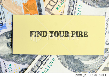 A yellow card with the inscription FIND YOUR FIRE is placed on a background of United States dollar bills, symbolizing motivation and financial aspirations A yellow card with the inscription FIND YOUR FIRE is placed on a background of United States dollar bills, symbolizing motivation and financial aspirations 135014011