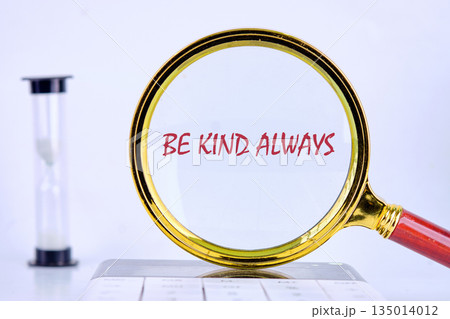 The motivational phrase BE KIND ALWAYS is magnified. A golden magnifying glass sits on a white surface next to an hourglass, suggesting the importance of kindness over time 135014012