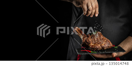 Chef seasoning grilled tomahawk steak with salt on dark background, copy space Chef seasoning grilled tomahawk steak with salt on dark background, copy space 135014748