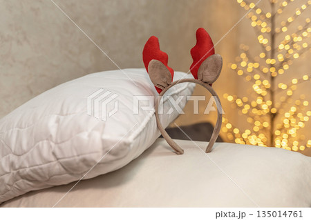 Christmas reindeer antler headband on white pillows with festive lights in background 135014761