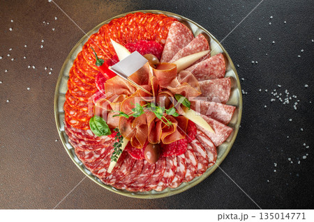 Assorted charcuterie platter with salami, prosciutto, chorizo, cheese, and olives on a rustic background, top view Assorted charcuterie platter with salami, prosciutto, chorizo, cheese, and olives on a rustic background, top view 135014771