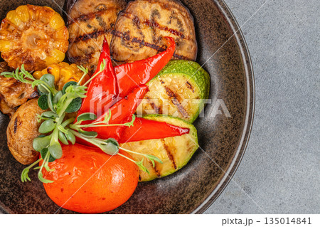 Grilled vegetables with corn, peppers, and zucchini on a dark plate 135014841