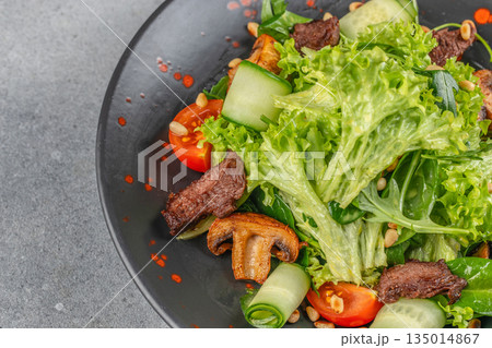 Fresh salad with grilled beef, lettuce, mushrooms, cucumbers, and tomatoes on a black plate with copy space 135014867