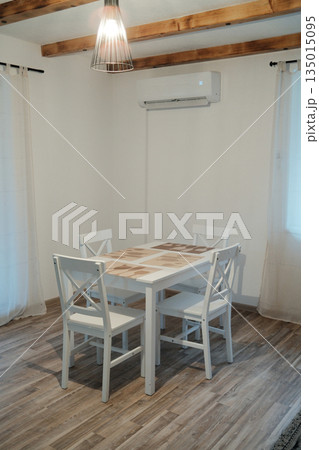 Minimalist dining area with white wooden table and chairs in a bright apartment interior. Clean composition reflects simplicity comfort and everyday home lifestyle 135015095