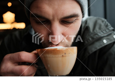 Close up of a man drinking cappuccino in a cozy cafe. The image captures focus, aroma and a peaceful coffee moment Close up of a man drinking cappuccino in a cozy cafe. The image captures focus, aroma and a peaceful coffee moment 135015185