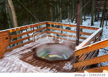 Snowcovered wooden deck showcasing cozy hot tub in nature 135015510
