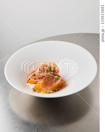 Thin prosciutto slices arranged elegantly over vibrant citrus sections Thin prosciutto slices arranged elegantly over vibrant citrus sections 135015681