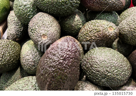 Avocados are arranged in a market display, showcasing their natural texture. The scene captures shoppers browsing for fresh produce in the afternoon 135015730