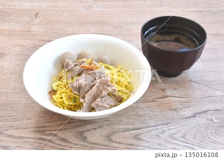 dry boiled Chinese yellow egg noodles with slice beef and meatball topping fried chop garlic on bowl with clear soup cup dry boiled Chinese yellow egg noodles with slice beef and meatball topping fried chop garlic on bowl with clear soup cup 135016108