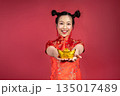 Portrait of smiling woman holding gold yuanbao toward camera on red background Portrait of smiling woman holding gold yuanbao toward camera on red background 135017489