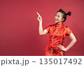 Happy Asian woman in Cheongsam pointing finger at copy space on red background. Happy Asian woman in Cheongsam pointing finger at copy space on red background. 135017492