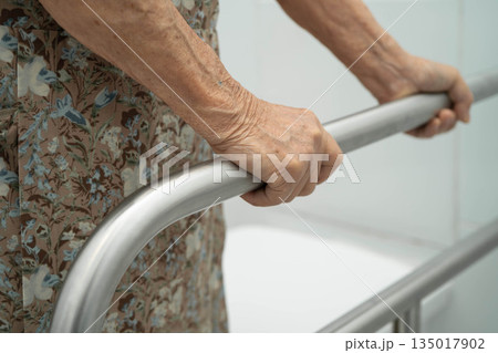 Asian elderly woman patient use handrail safety in toilet support rail in bathroom. 135017902