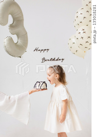 A young girl is about to eat a birthday cake, with balloons and a 'Happy Birthday' sign in the background. A young girl is about to eat a birthday cake, with balloons and a 'Happy Birthday' sign in the background. 135018281