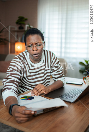 Black woman concentrating on important financial report at home office Black woman concentrating on important financial report at home office 135018474