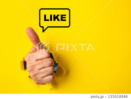 Hand giving thumbs up through torn paper with like speech bubble Hand giving thumbs up through torn paper with like speech bubble 135018846