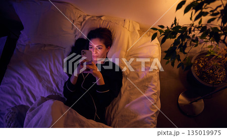Woman using smartphone in bed at night with screen light. 135019975