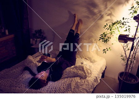 Overhead view of woman lying in bed and using smartphone. Overhead view of woman lying in bed and using smartphone. 135019976
