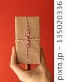 hand holding craft wrapped gift over red background 135020336