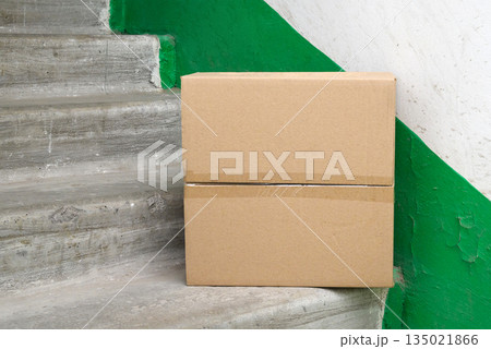 closed brown cardboard box on concrete steps in a house entrance hallway closed brown cardboard box on concrete steps in a house entrance hallway 135021866