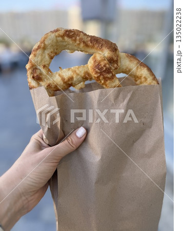 Hand holding fresh pretzel in paper bag outdoors on city street background 135022238