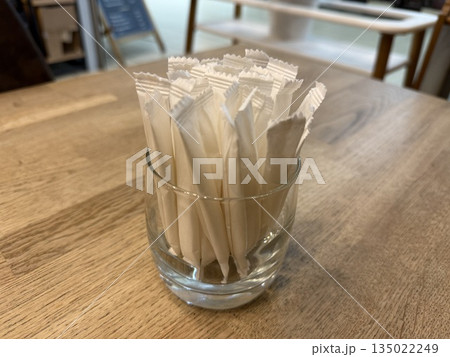 Glass filled with individually wrapped sugar packets on a wooden table background Glass filled with individually wrapped sugar packets on a wooden table background 135022249