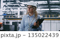 Factory Floor Management, Female Engineer Wearing White Hard Hat and Checking Data 135022439