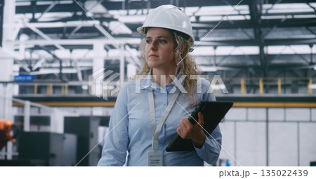 Factory Floor Management, Female Engineer Wearing White Hard Hat and Checking Data Factory Floor Management, Female Engineer Wearing White Hard Hat and Checking Data 135022439
