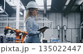 Female Industrial Specialist Wearing Hard Hat and Using Tablet to Monitor Operations 135022447