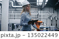 Female Industrial Specialist Wearing Hard Hat and Using Tablet to Monitor Operations 135022449