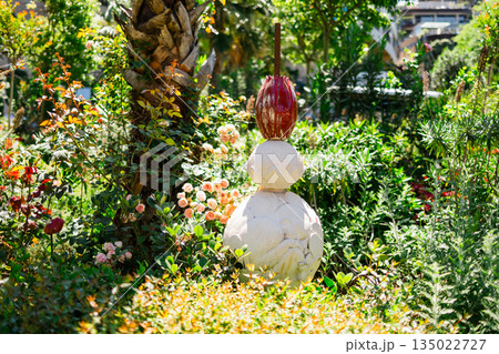 Decorative garden sculpture surrounded by lush greenery and flowering plants. Artistic landscape design, outdoor aesthetics, creative expression and serene residential garden atmosphere 135022727