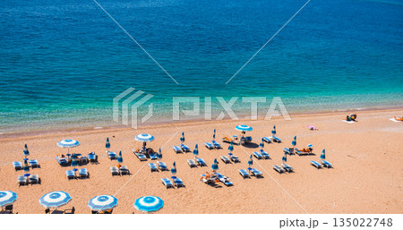 Organized pebble beach with umbrellas and loungers by the Adriatic Sea, banner. Summer tourism, coastal comfort, vacation routine, and relaxed seaside lifestyle in Budva, Montenegro Organized pebble beach with umbrellas and loungers by the Adriatic Sea, banner. Summer tourism, coastal comfort, vacation routine, and relaxed seaside lifestyle in Budva, Montenegro 135022748